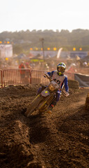 A motocross rider bending into a tight turn on a wet dirt track illuminated by the evening sunlight...