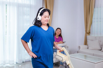 Woman cleaning with vacuum cleaner in the living room at home. Female vacuuming the floor with blurred friend using smartphone in background