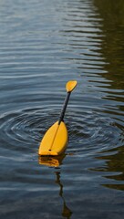 Close-up of a kayaker's paddle creating ripples in a tranquil lake.