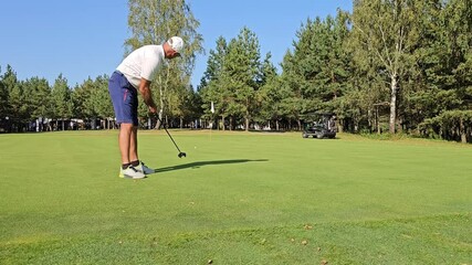 Man practices putting on a sunny golf course 