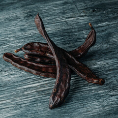 some ripe carob pods on a gray rustic table