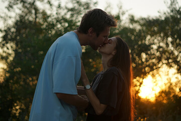 Fototapeta premium man and woman stand close to each other in a forest during sunset, the sun shining brightly behind the trees