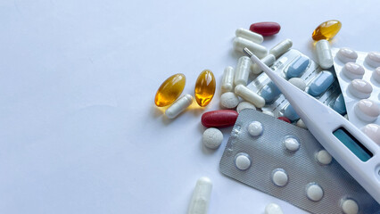 Assortment of multicolored pills, capsules, and a digital thermometer showcasing a normal temperature, set against a clean white background, ideal for health and medical use