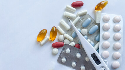 Assortment of multicolored pills, capsules, and a digital thermometer showcasing a normal temperature, set against a clean white background, ideal for health and medical use