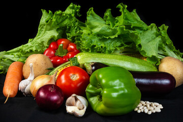 A vibrant assortment of fresh organic vegetables, including lettuce, tomato, pepper, garlic, and zucchini, displayed on a black background, symbolizing healthy eating and natural produce.