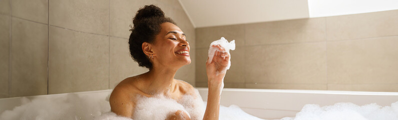 Woman bathes in foamfilled bathtub, smiling happily