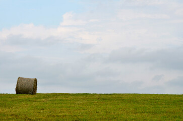 Single Hay Bale in field with clouds in sky during summer