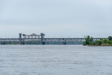 Fototapeta premium View on road and railway bridge through river. Panorama on bridge for train cargo and passenger transport. Architectural structure connecting left and right banks city. Infrastructure Dnipro Ukraine.