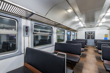 Obraz premium interior of an cheap empty train car with simple bench-style seating. The car features metal luggage racks above the windows, a clean, minimalist design, and a bright, neutral color scheme.