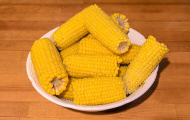 yellow boiled corn in a white plate on a wooden table