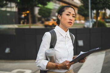 Mature japanese woman walk with backpack thermos and clipboard outdoor