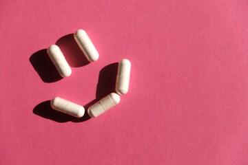 The pills are laid out as a smiley face on a pink background. Medications. Concept: successful treatment, recovery. Vitamins. 