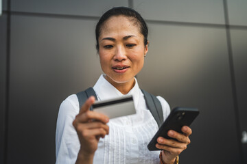 japanese woman buy online on cellphone with credit card on black wall