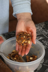 A woman is making healthy cookies. With nuts and chocolate. She is shaping the dough.