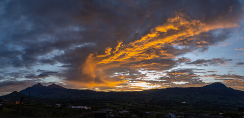 Spectacular Andean sunset with the silhouette of the Ilinizas and Corazon volcanoes under reddish and gray clouds.