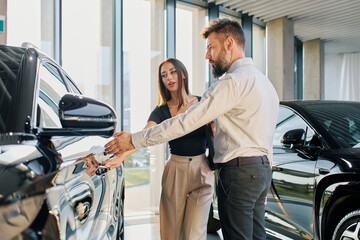 A couple of a man and a woman walk around a car dealership and choose a car