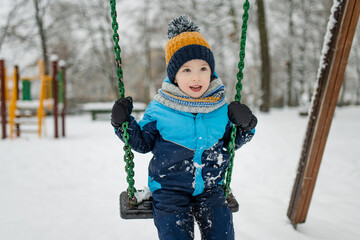 Adorable little boy having fun on a playground on snowy winter day. Cute child wearing warm clothes playing in a snow.