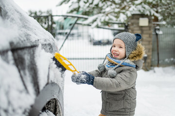 Adorable little boy helping to brush a snow from a car. Mommy's little helper. Winter activities for kids.