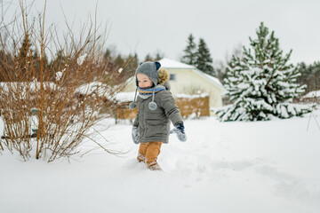 Adorable little boy having fun on snowy winter day. Cute child wearing warm clothes playing in a snow.