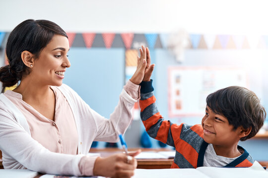 High five, teacher and kid at desk in classroom for support in student growth, child development and education. Learning, woman and boy with winning celebration, praise or motivation at middle school