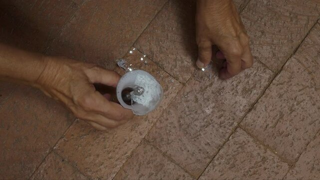 A woman picking up glass pieces from a broken light bulb