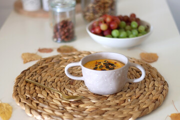 Pumpkin and potato creamy soup, bowl of grapes, jars of nuts and autumn leaves on the table. Selective focus.