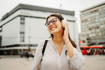 Fototapeta premium Young caucasian woman listening to music or audio book in the city