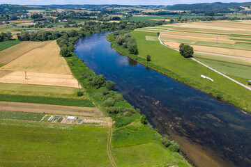 Naklejka premium Aerial view of a tranquil river winding through vibrant green fields and farmland, showcasing the beauty of the rural landscape.