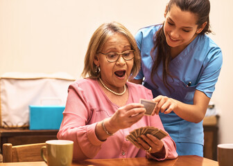 Elderly, woman and caregiver with playing cards for fun, memory exercise or happy company in...