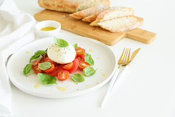 Salad Caprese with tomato, cherry, mozzarella and basil leaves on white wooden table