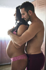 Fototapeta premium Home, hug and pregnant with couple, stomach and wellness with parents, support and bonding together. Healthy, pregnancy and man with woman, embrace and relationship with marriage, happiness and tummy