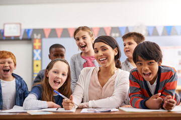 Portrait, teacher and group of happy kids in class for support in growth, child development and lesson for education. Learning, woman and students at desk with notes, smile and fun elementary school