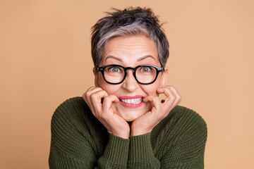 Photo of horrified woman with short hairdo dressed khaki sweater in glasses biting fingers staring isolated on beige color background