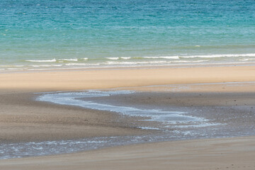 Fine sandy beach in front of a calm and clear turquoise blue sea.