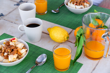 Gedeckter Frühstückstisch auf gefliesten Tisch mit Müsli in schüsseln Frisch gepressten Orangensaft, Kaffee, Orangen, Zitronen auf grünen Untersetzer Matten