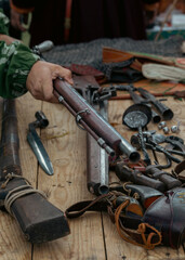 Set of antique firearms, bayonets, saber and peak tips on wooden table. Human hand holds a rifle, selective focus.