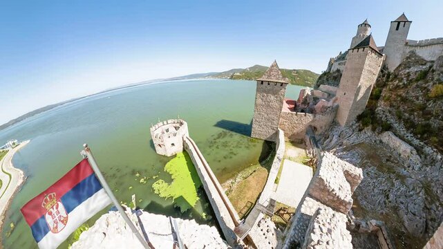 Aerial view of Golubac fortress, a medieval structure, stands majestically on the banks of Danube river. A Serbian flag waves proudly, adding a touch of patriotism to the scene