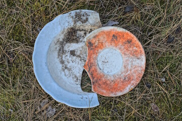 two old dirty colored broken plates lie on dry grass and ground on a summer street