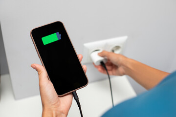 Lady holding cellphone while putting on charging into wall outlet. Charging phone with regular...