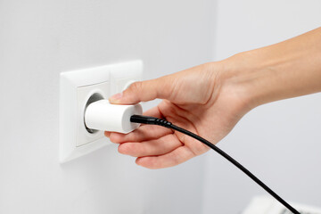 Woman inserting plug into an outlet, plugging phone charger into the socket, closeup shot