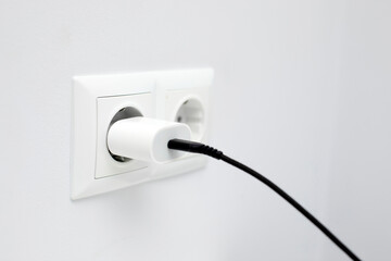 Closeup up of charger adapter plugged in power socket indoors. Concept of charging devices