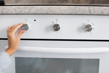Woman adjusting modern white electric oven in kitchen, turning on and setting temperature, closeup