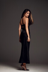 Fototapeta premium Rear view of a sensual female model in a black long dress , posing in studio