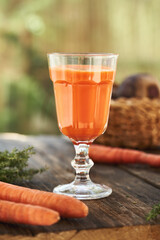 A glass of fresh carrot juice on a wooden table outdoors