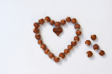 Heart made of hazelnuts in shell and wooden heart, white background