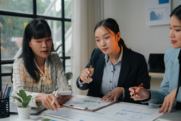 Three female executives in a meeting, analyzing financial data and utilizing a calculator to strategize for the future