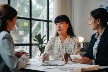 Three asian businesswomen collaborating at a desk, analyzing financial data, and strategizing for a new business venture