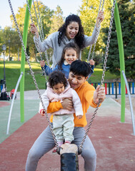 Front view of hispanic family enjoying a big swing in a playground