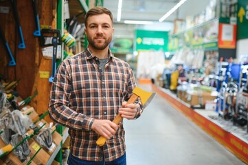 A young handsome man buys an ax in a hardware store