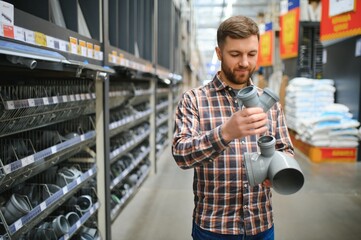 Handsome man choosing sewer pipes standing near the showcase of the plumbing shop